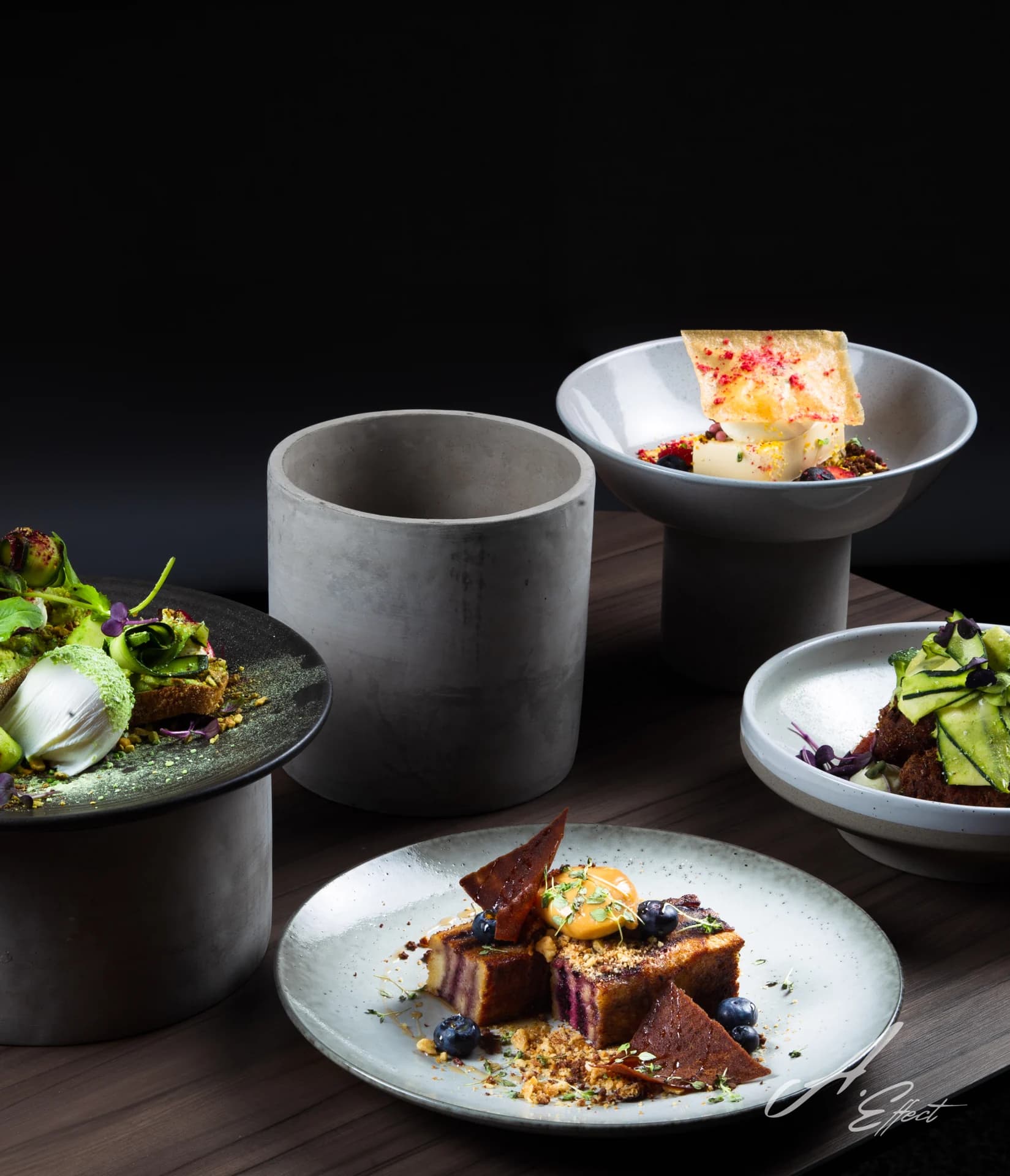 A collection of plated dishes arranged with dark ceramic cups