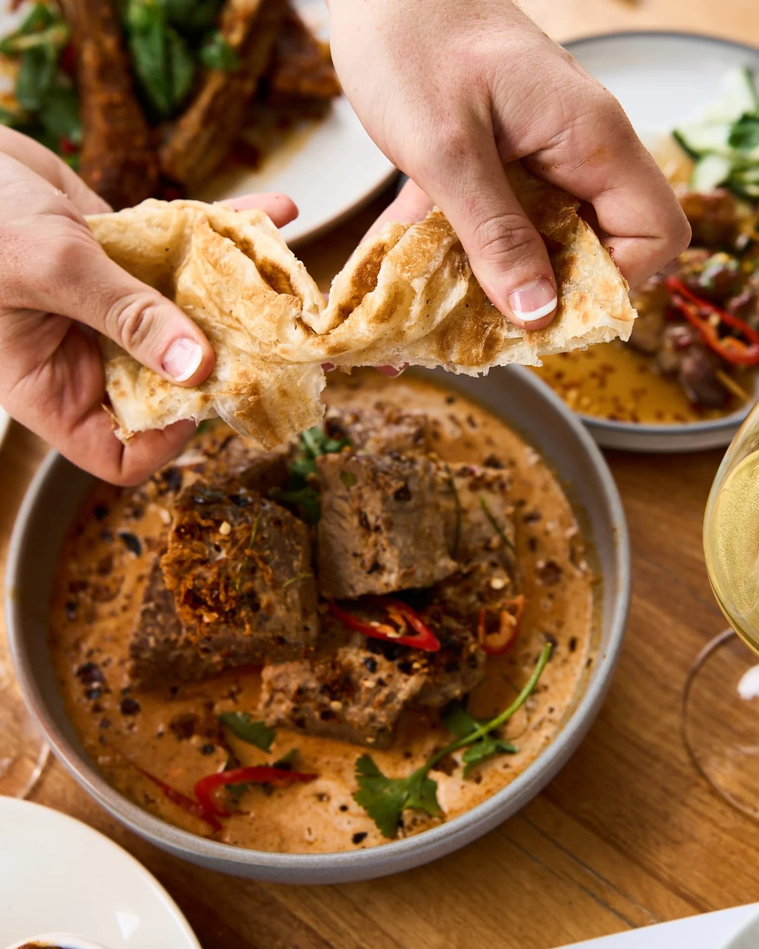 Hands dipping bread into a bowl of food