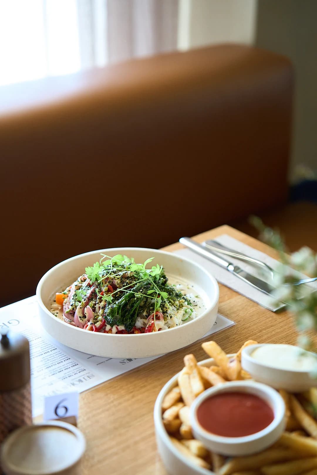 A bowl of food and iced drink beside a sunlit café window